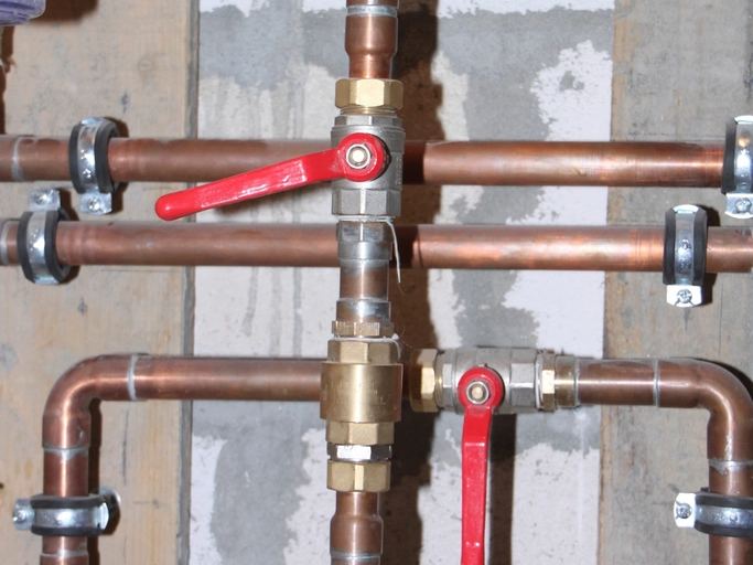 Copper water pipes with red-handled shut-off valves on a wall