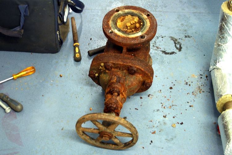 A badly corroded cast-iron gate valve with its handwheel, lying on a workshop floor