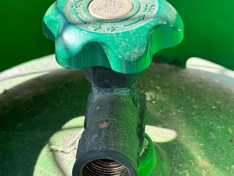 The valve and outlet on top of a green gas cylinder