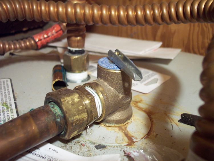 Brass relief valve on top of a water heater, with rust stains where it has dripped