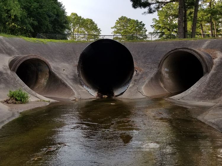 Three concrete stormwater culverts emptying into a lined channel under trees